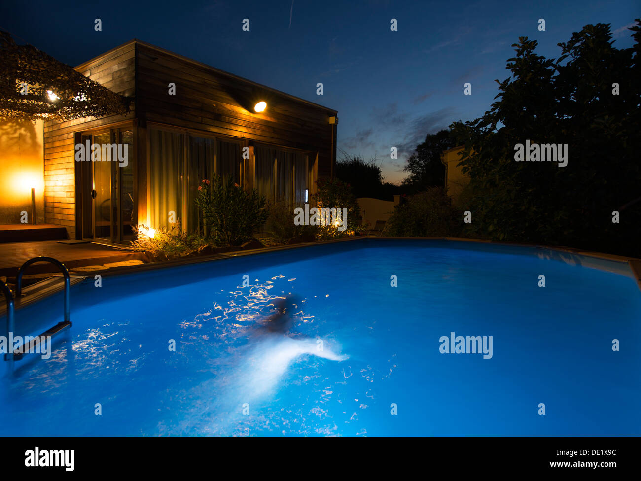 Woman swimming in a lit outdoor swimming pool at night Stock Photo