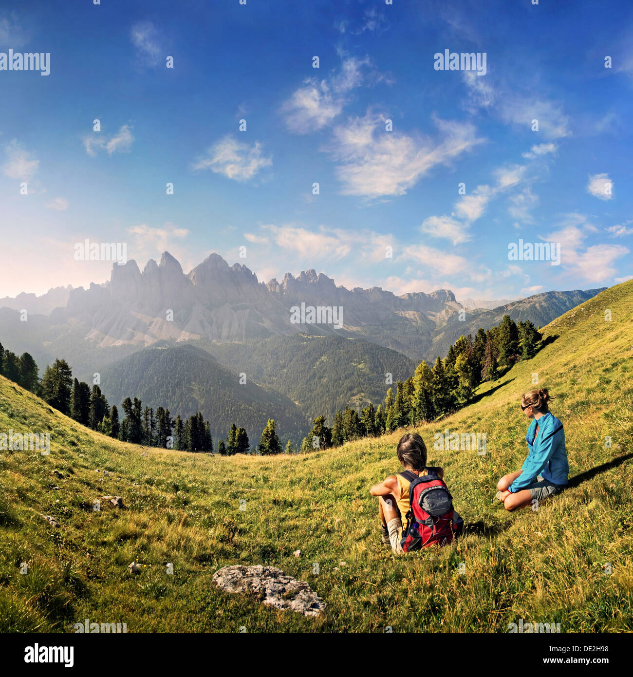Hikers relaxing in a meadow enjoying the view of the Geisler group, Aferer Geisler mountains, Villnoesstal valley Stock Photo