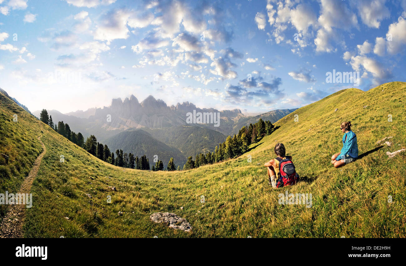 Hikers relaxing in a meadow enjoying the view of the Geisler group, Aferer Geisler mountains, Villnoesstal valley Stock Photo