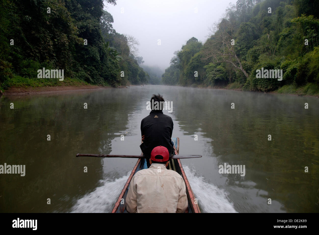 Solitary wooden boat floating upstream on the Nam Ou River, mist and jungle on the river bank, Ban Sopkang, Phou Den Din Stock Photo