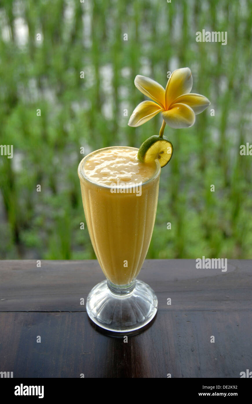 Soft drink, mango smoothie in a glass decorated with flowers, in front of a rice field in Ubud, Bali, Indonesia, Southeast Asia Stock Photo