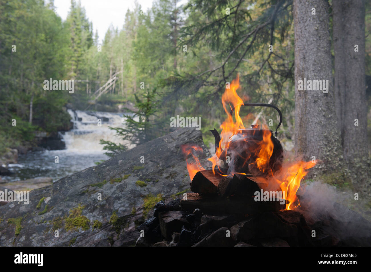 Water is boiled in the wilderness, coffee kettle on an open fire, flames and smoke, Fulvan river, Tjaernvallen near the Stock Photo