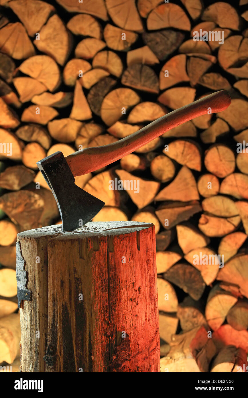 Axe on a log, stacked firewood at the back Stock Photo