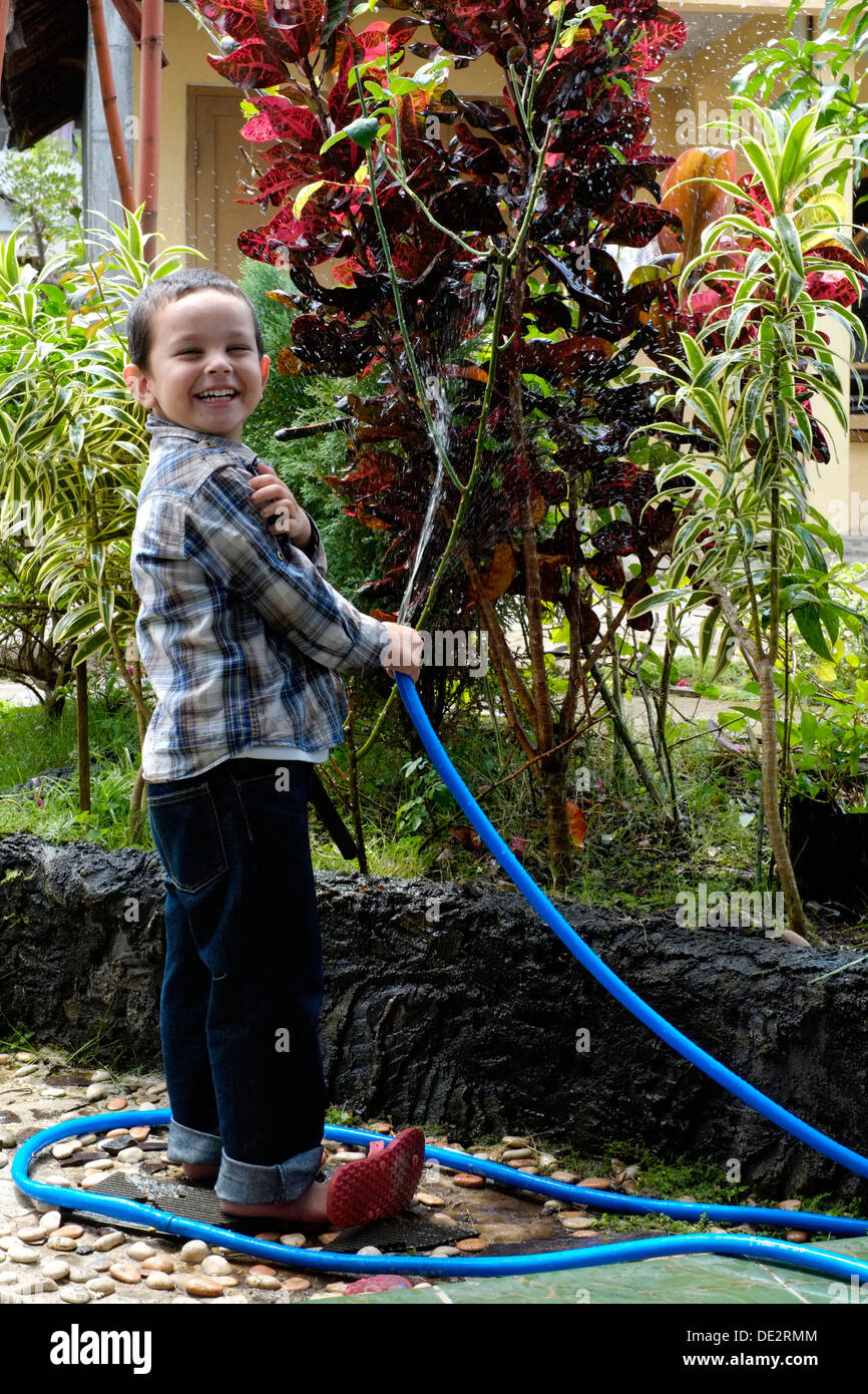 smiling happy little boy watering the garden using a hosepipe java indonesia Stock Photo