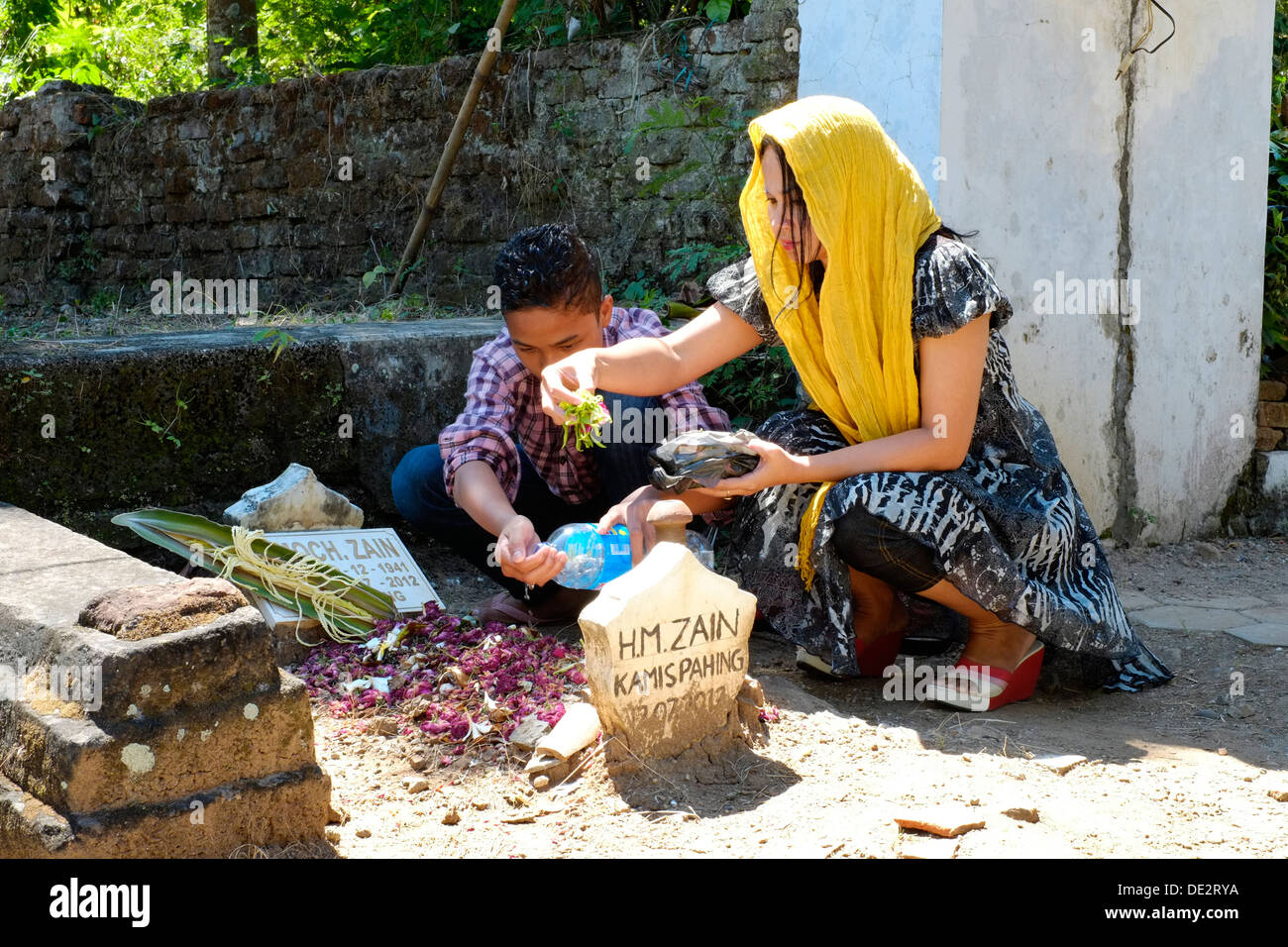 indonesian woman tends to pays her respects and prays at her fathers grave accompanied by her son Stock Photo