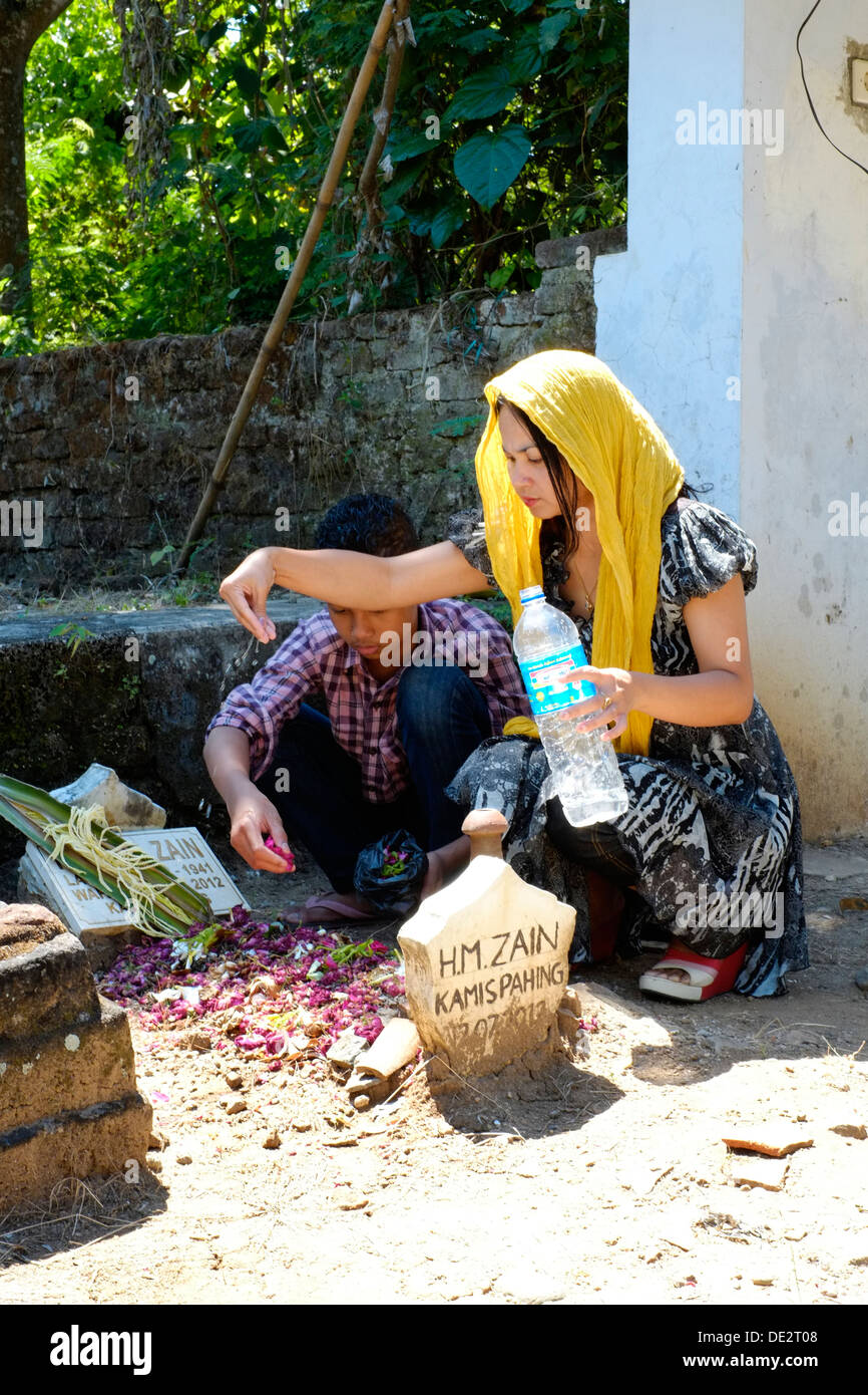 indonesian woman tends to pays her respects and prays at her fathers grave accompanied by her son Stock Photo