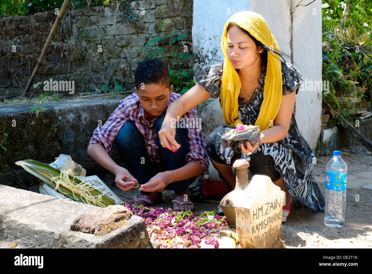 indonesian woman tends to pays her respects and prays at her fathers grave accompanied by her son Stock Photo