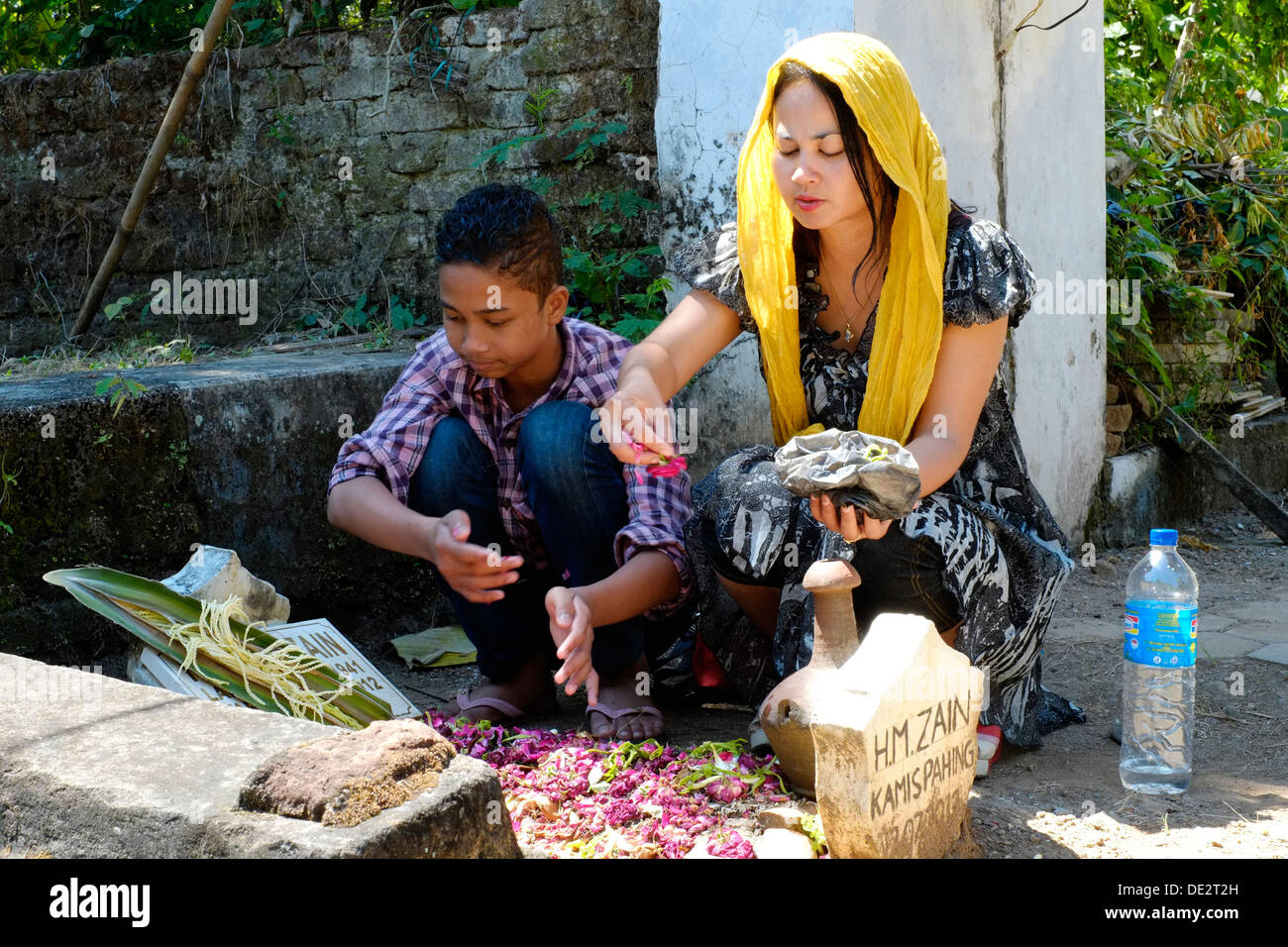 indonesian woman tends to pays her respects and prays at her fathers grave accompanied by her son Stock Photo