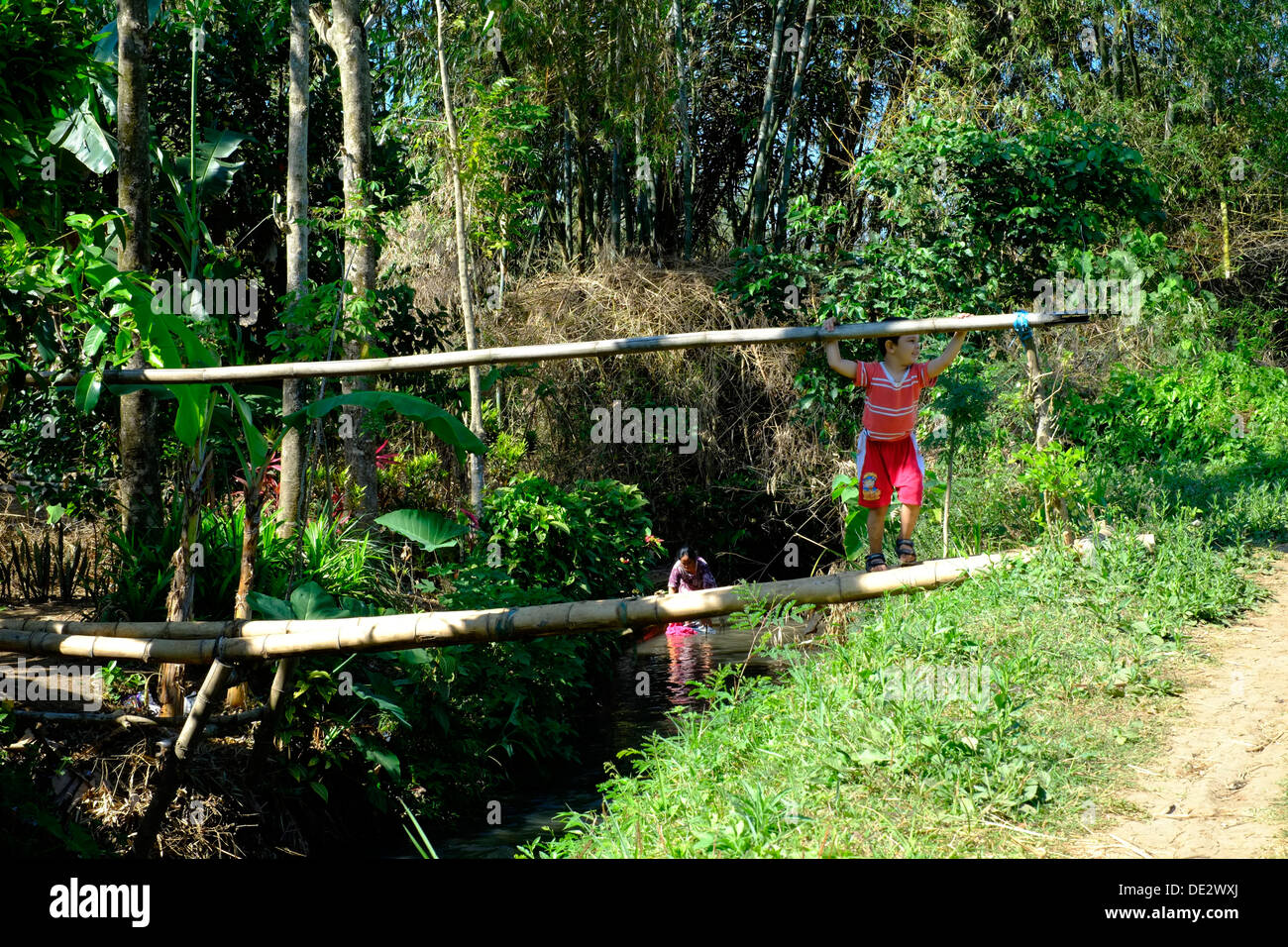 little boy playing on a rickety bamboo bridge over small river in rural village java indonesia Stock Photo