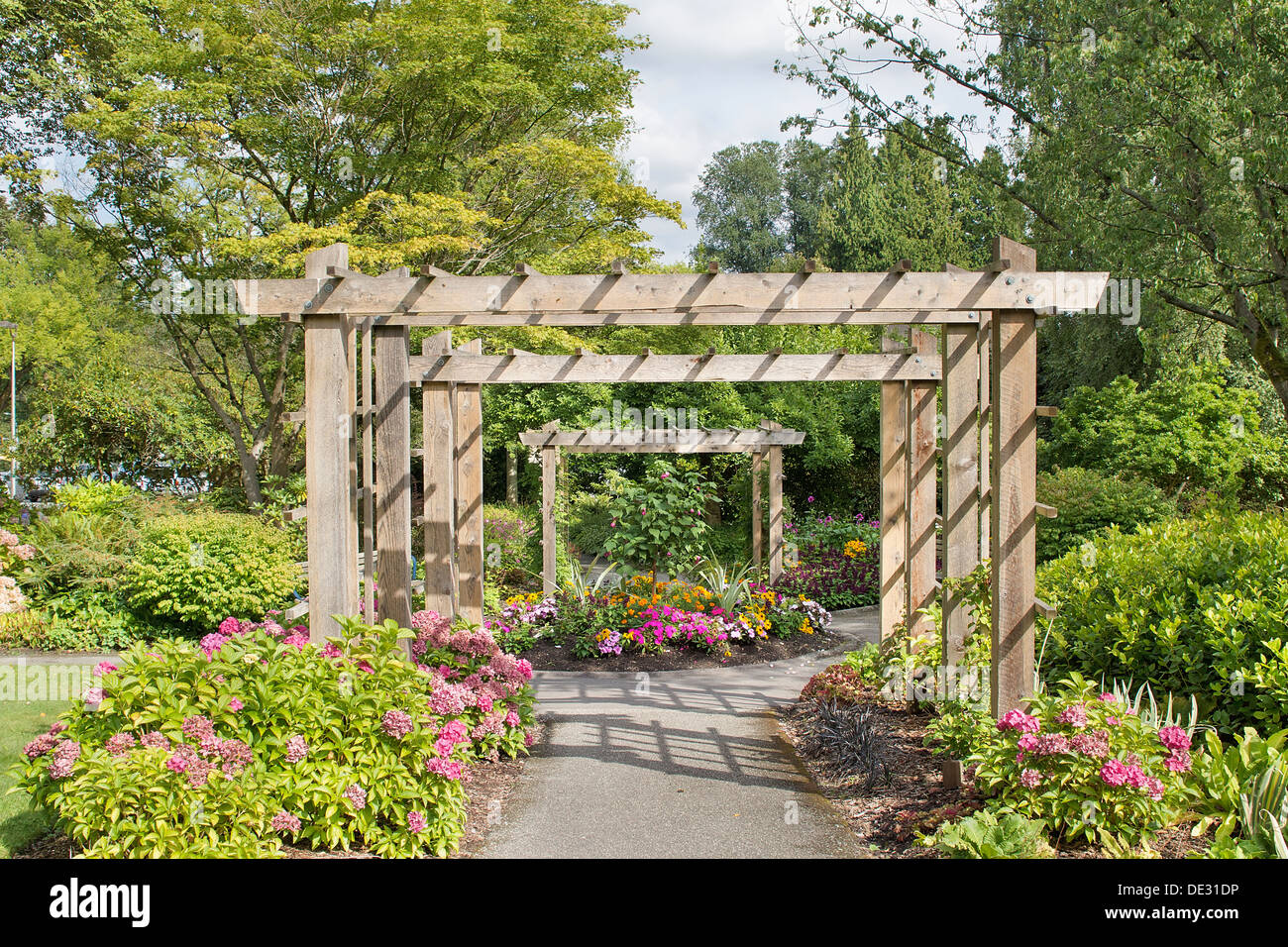 Wood Arbor Over Garden Path with Plants Trees and Flowers Blooming in Summer Stock Photo