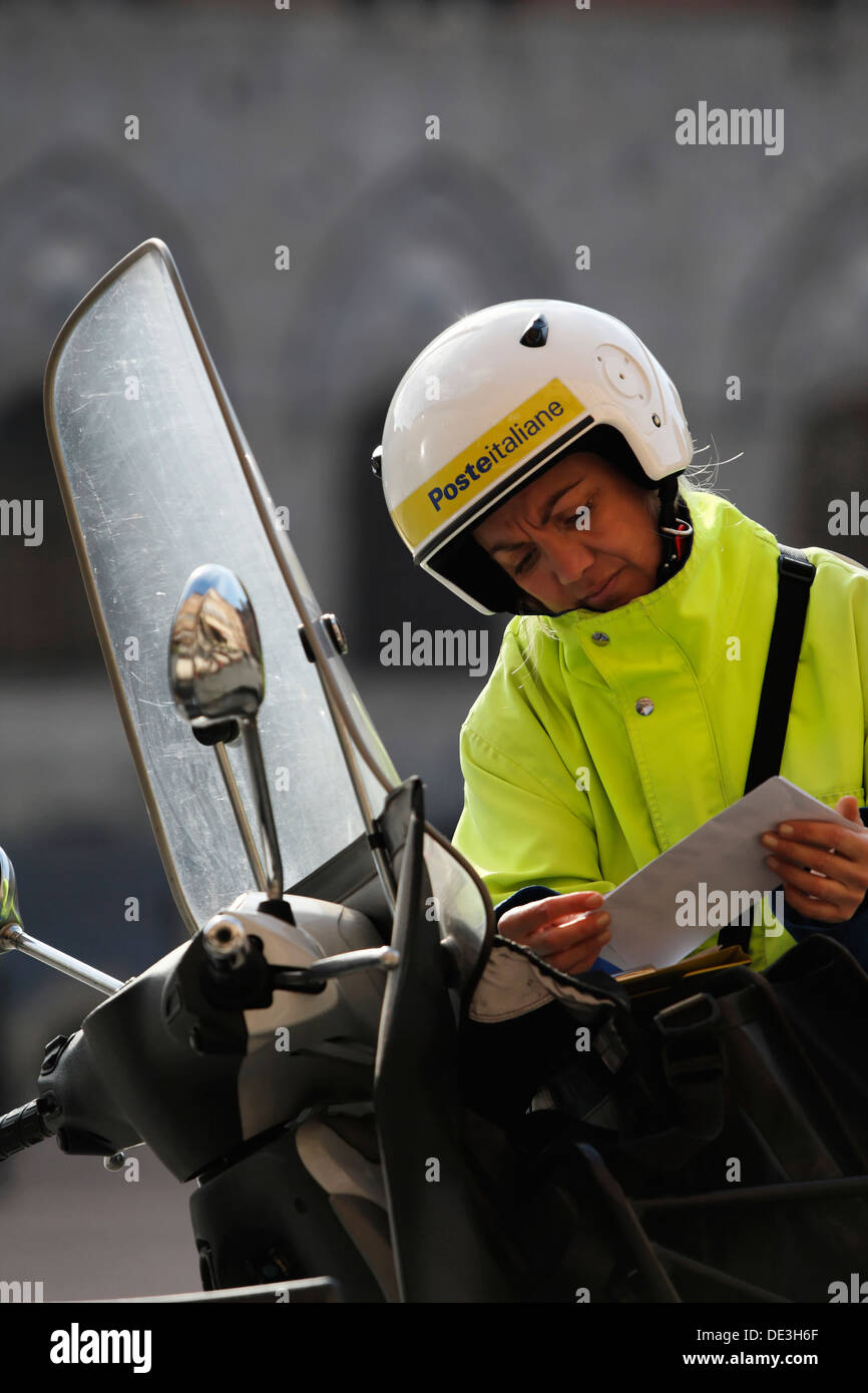 Woman Italian postal worker (Posteitaliane ) reading mail whilst wearing a  motor bike crash helmet,Siena Tuscany Italy Stock Photo - Alamy