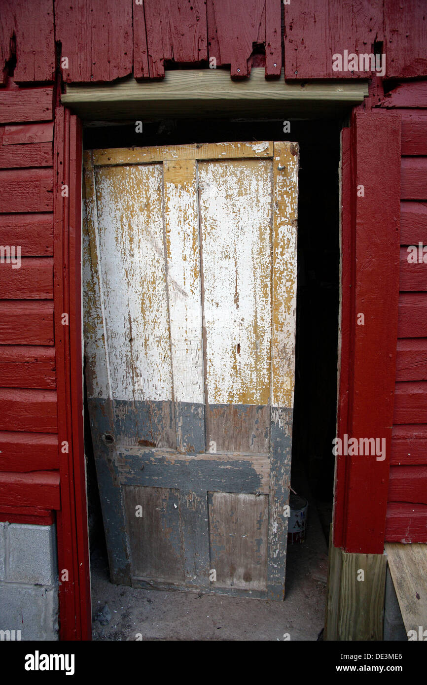 An old barn door with chipped paint. The door has fallen off it´s hinges, and rests inside the barn as a mediocre barrior Stock Photo