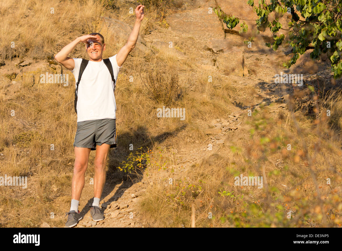 Male backpacker standing waving on a mountains slope with a broad smile to show his enjoyment of hiking in nature in the summer Stock Photo