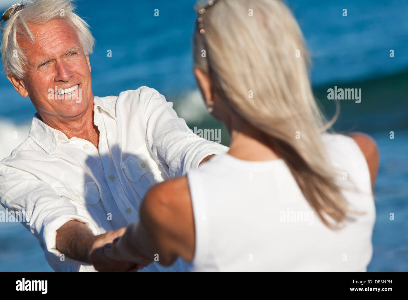 Happy senior man and woman couple dancing and holding hands on a deserted tropical beach blue sea Stock Photo