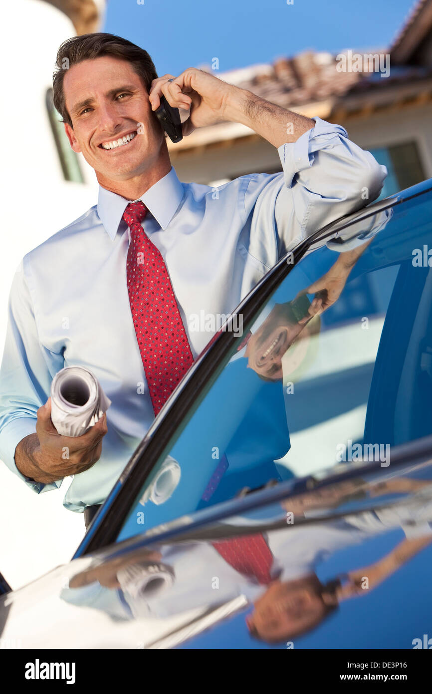 A successful businessman or architect holding plans & talking on his cell phone by a car Stock Photo