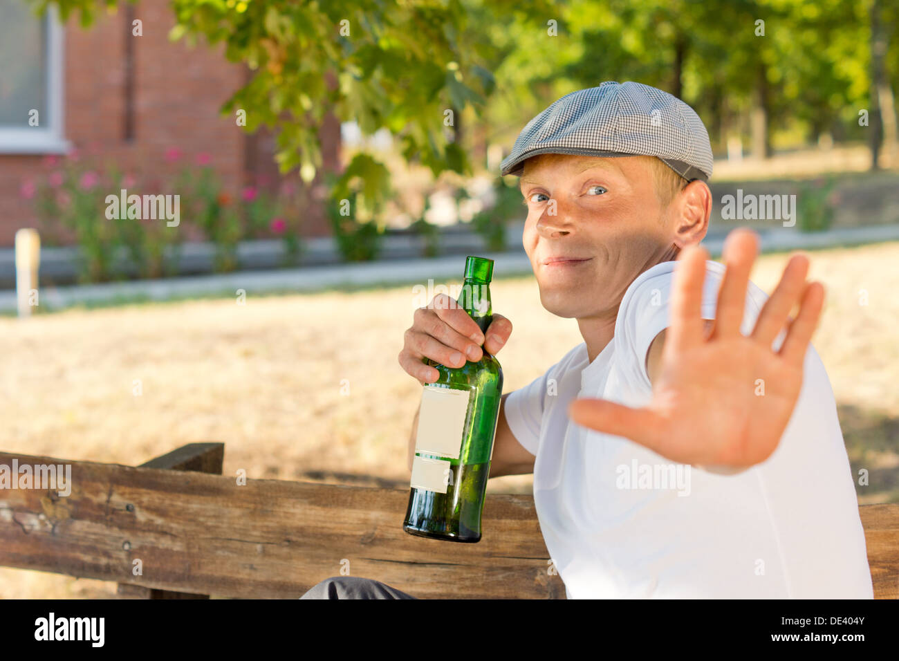 Alcoholic protecting his privacy pushing out his hand in a Stop gesture while pulling back with his bottle of booze Stock Photo