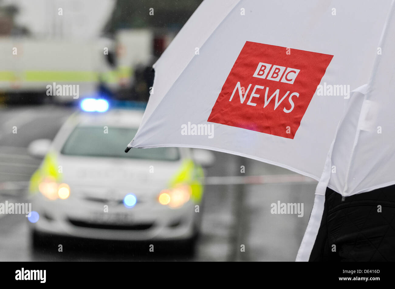 Ballyclare, Northern Ireland. 11th September 2013 -  Journalist holds a BBC News umbrella while watching police and army activity Credit:  Stephen Barnes/Alamy Live News Stock Photo
