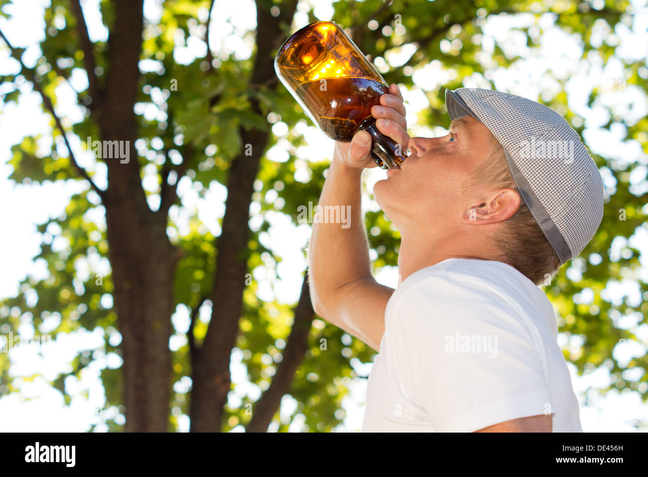 Profile portrait of a middle-aged man drinking from a bottle outdoors with blurred branches and foliage in the background Stock Photo