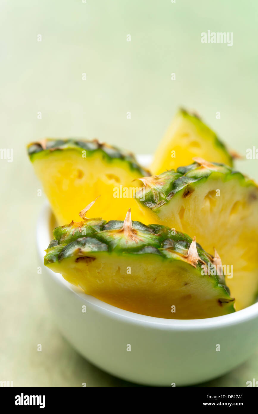 Four pieces of freshly cut, delicious and appetizing pineapple sat in a white bowl on a bright green wooden surface Stock Photo