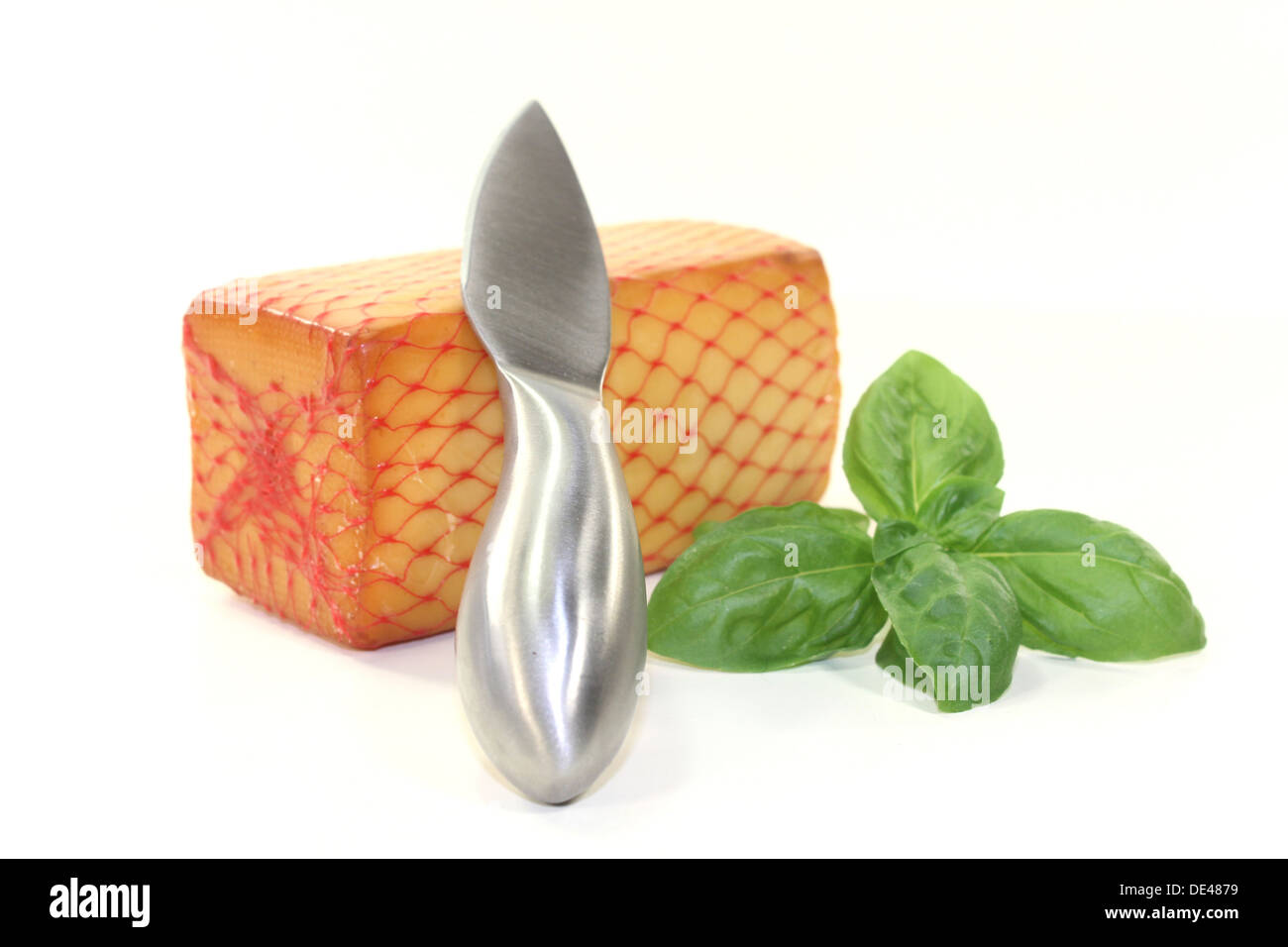 a piece of cheese with a cheese knife and basil Stock Photo