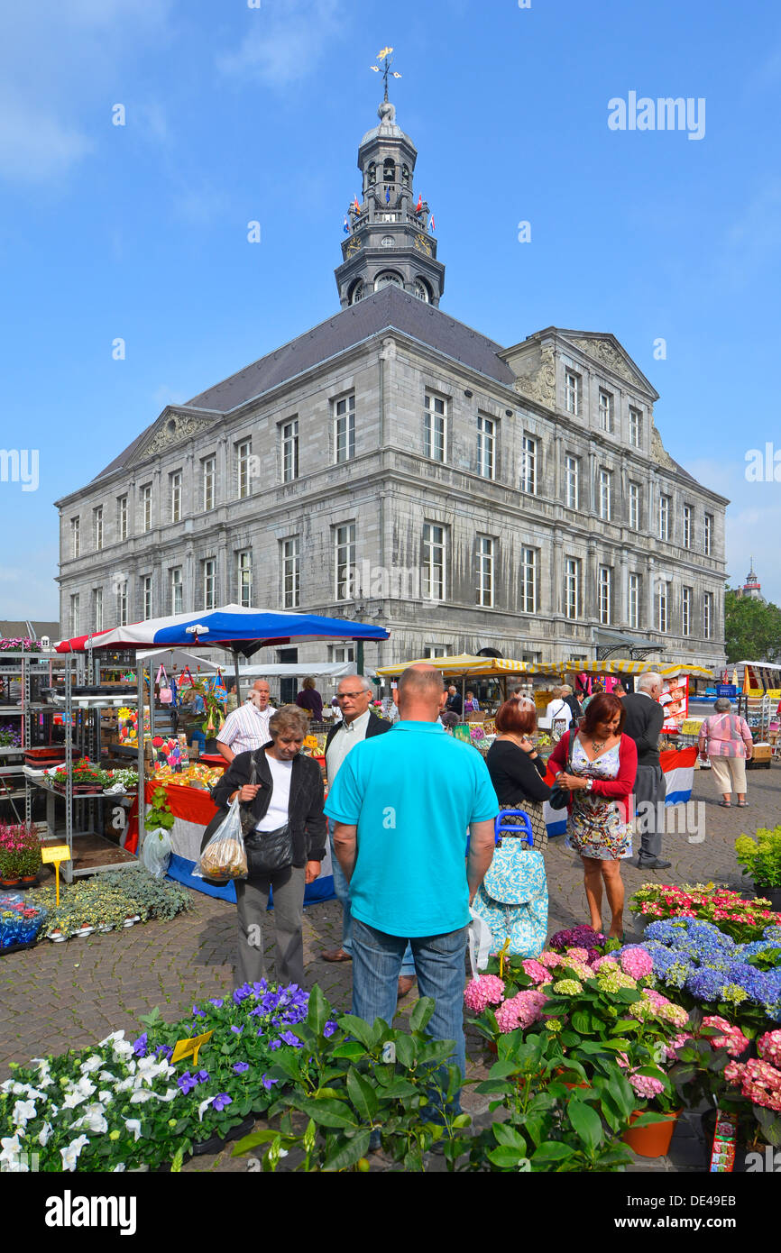 Maastricht market square overlooked by historical Town Hall flower sellers at work & shoppers viewing flowers for sale in sunny Limburg Netherlands EU Stock Photo