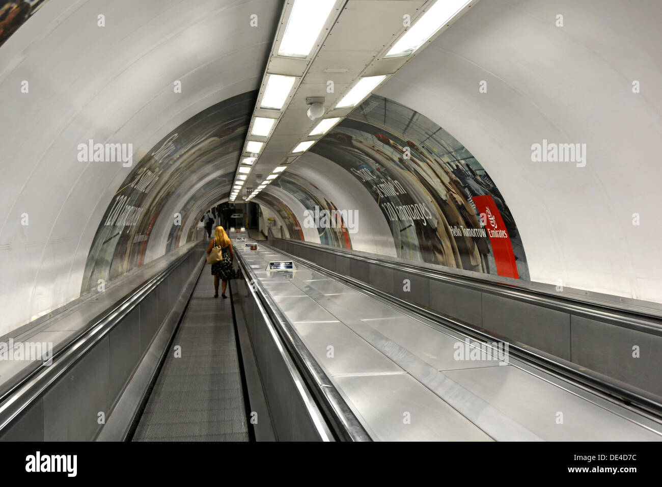 Woman on travelator moving pavement in tunnel leading to underground train platform London England UK Stock Photo