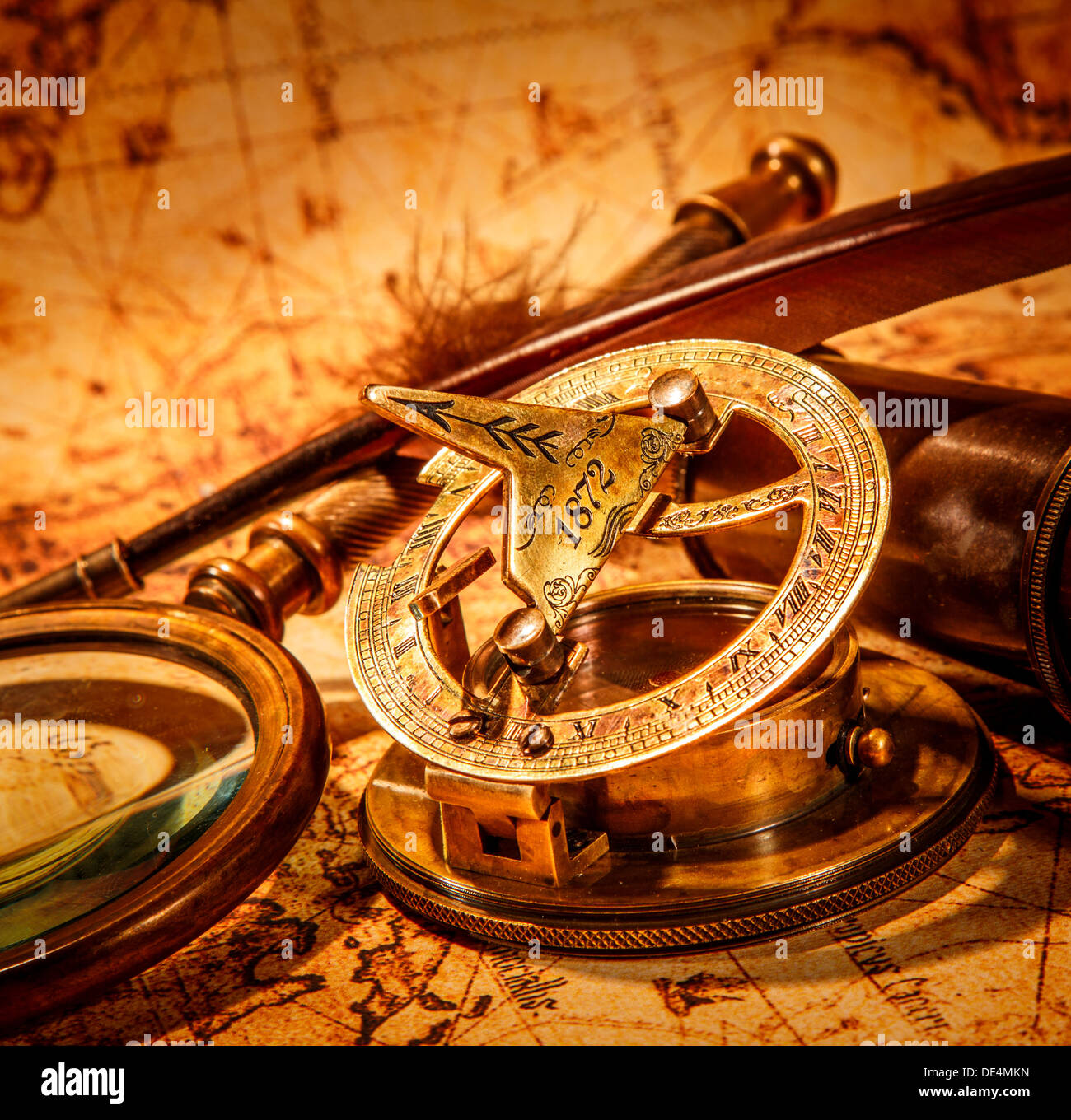 Vintage compass, goose quill pen, spyglass and a pocket watch lying on an old map. Stock Photo