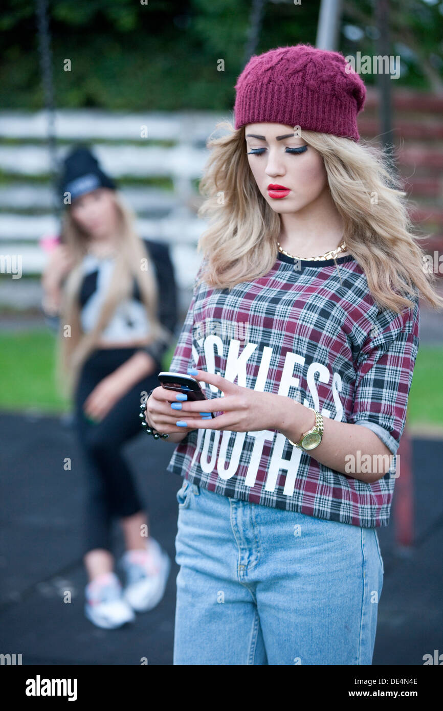 Teenage girl checking mobile phone in park with another girl out of focus in the background. Stock Photo