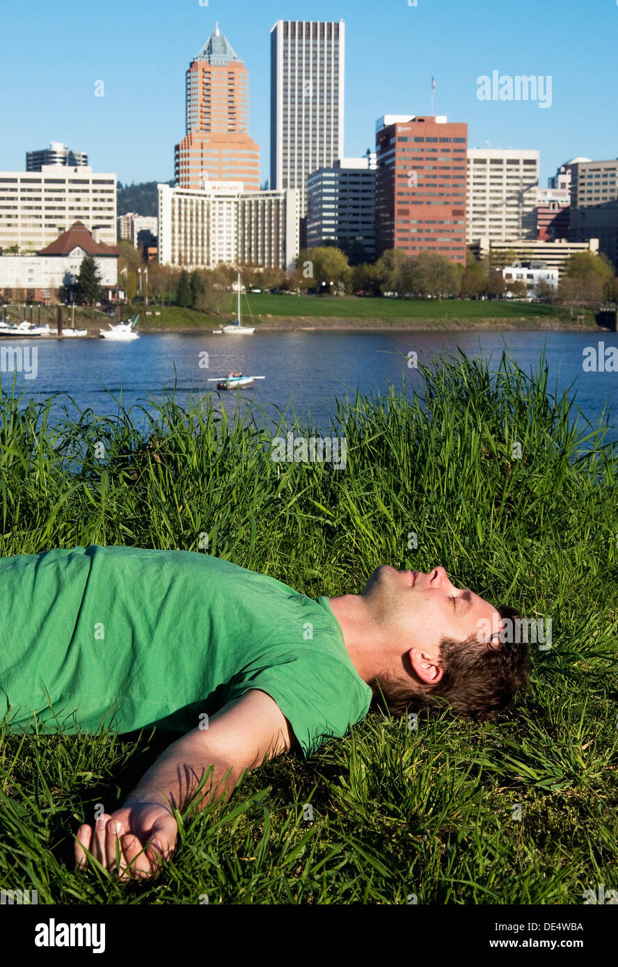 A man laying in the grass on the eastern bank of the willamette river in Portland, Oregon. Stock Photo