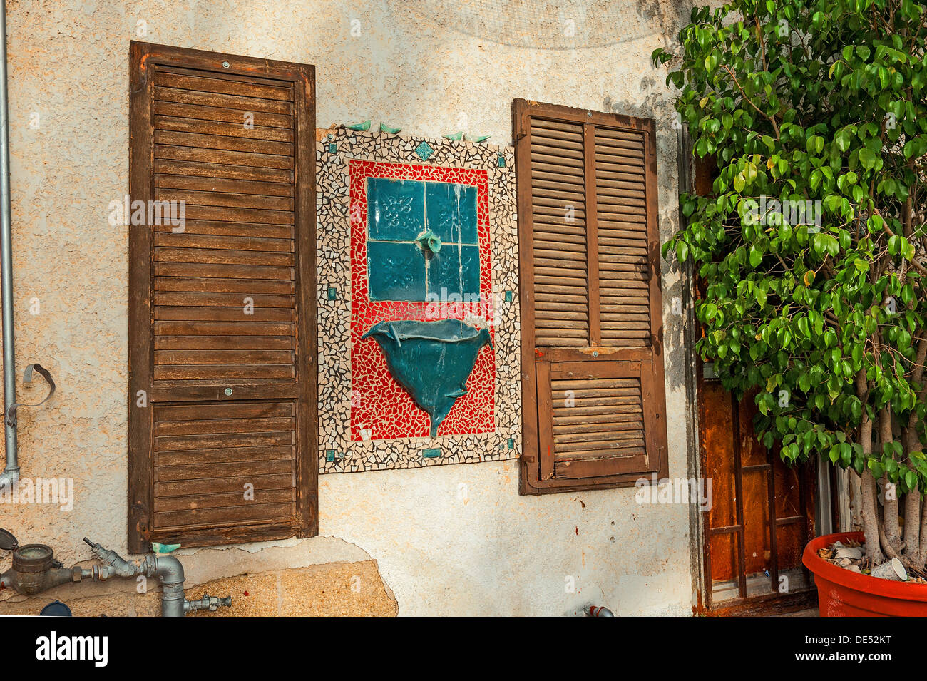 A building wall with mosaics, water fountain fake shutters and pipes in Mazkeret Batya Israel Stock Photo