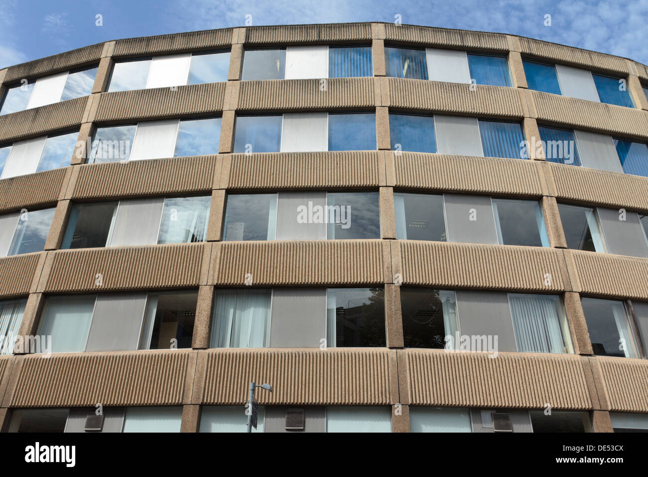 Windows reflecting sky in a 1960s curved reinforced concrete Brutalist office building with ribbed concrete panels in Bristol. Stock Photo