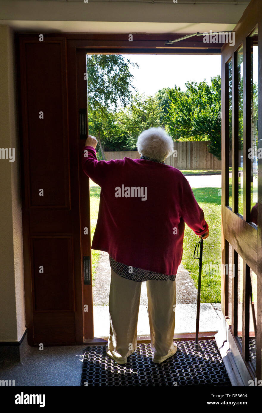 ELDERLY ALONE FRONT DOOR WAITING UNSURE Pensive elderly senior old age lady standing alone with walking stick pauses at her open apartment front door Stock Photo