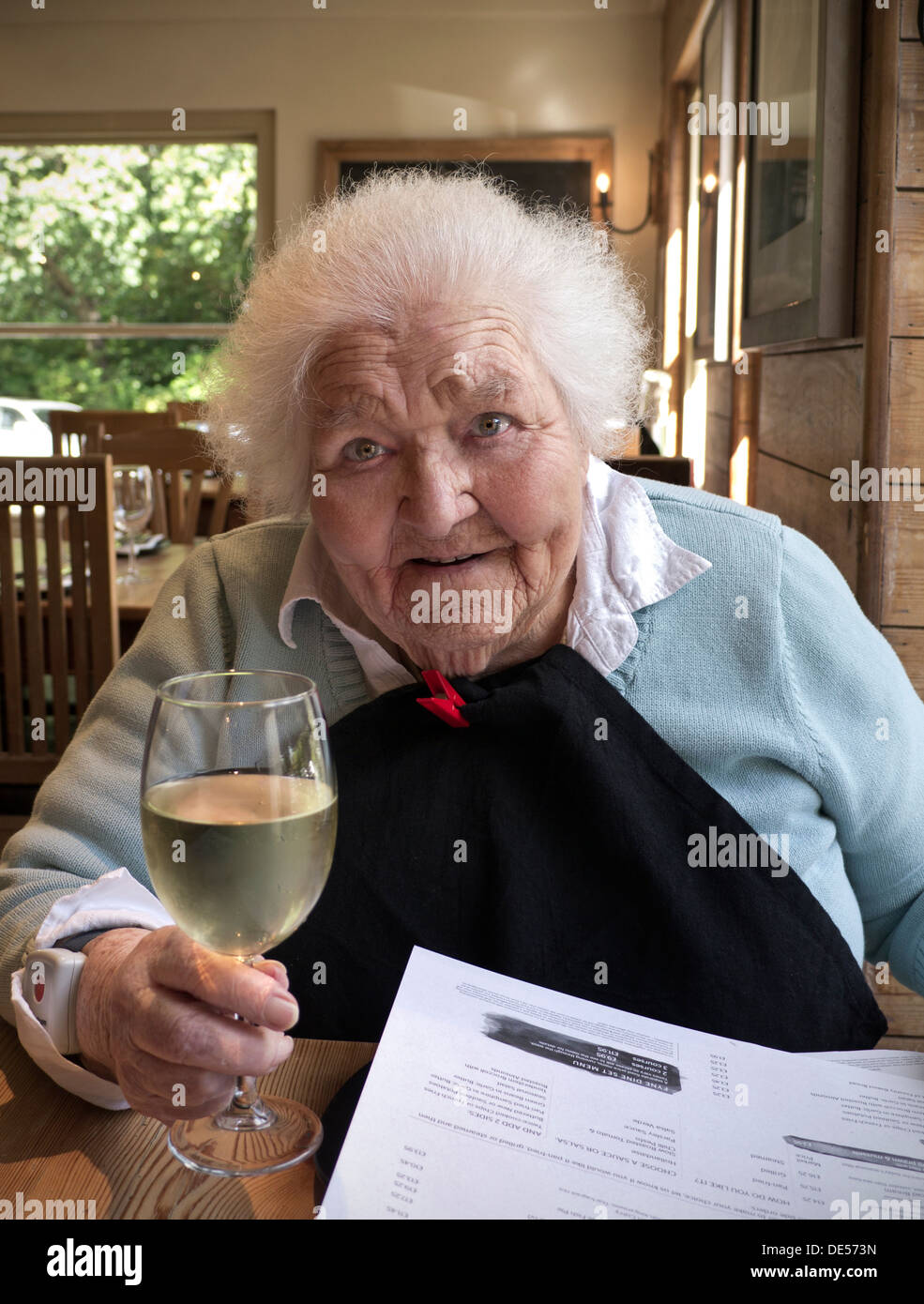Happy elderly lady in her 90s enjoying a glass of white wine in a restaurant Stock Photo
