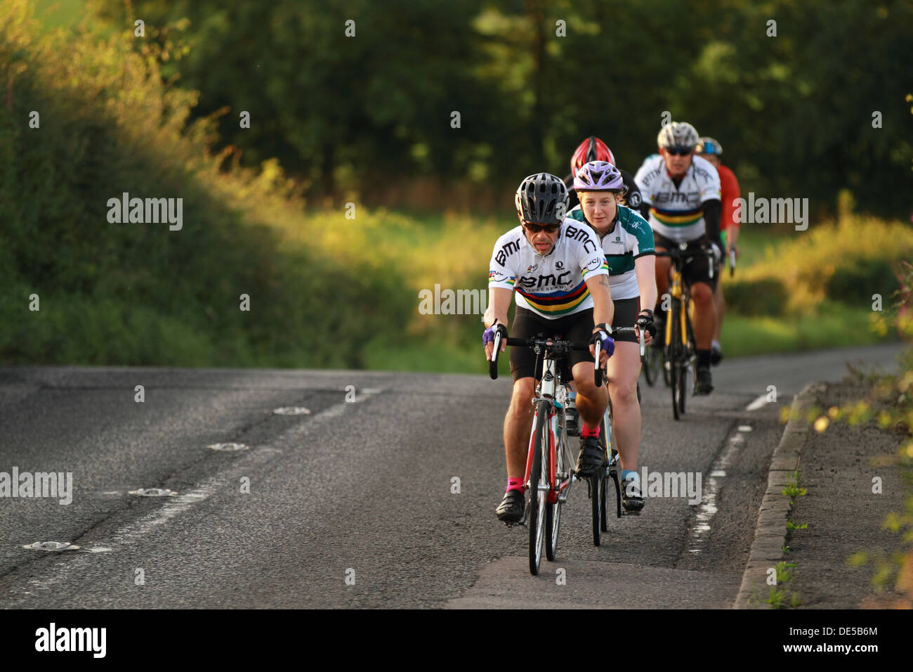 A group of professional road cyclists travel down a quiet country road at dusk. B822, Glasgow, Scotland, UK Stock Photo