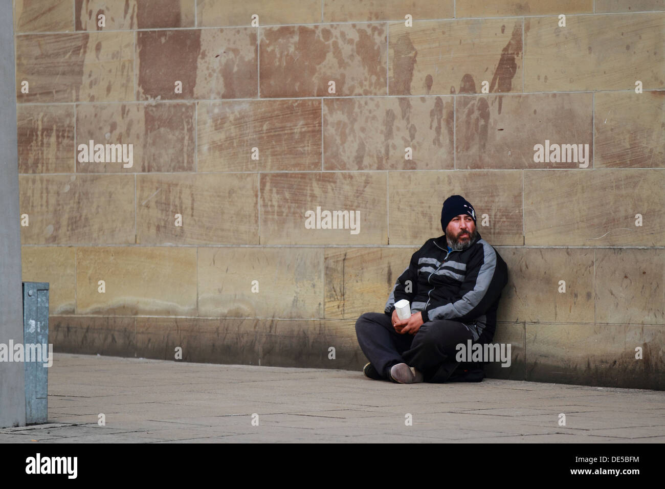 A homeless man begs for money at the side of the street. Poor penniless starving foreign beard Stock Photo