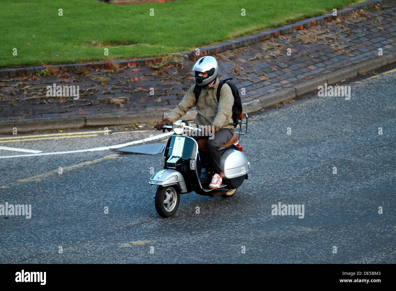 A man on a moped scooter bike travels to work wearing a helmet and plain clothing Stock Photo