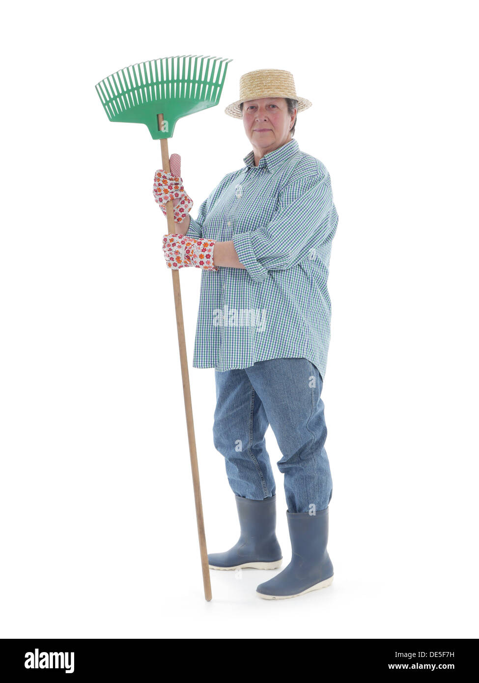 Senior woman gardener wearing straw hat and rubber boots posing with rake over white background Stock Photo