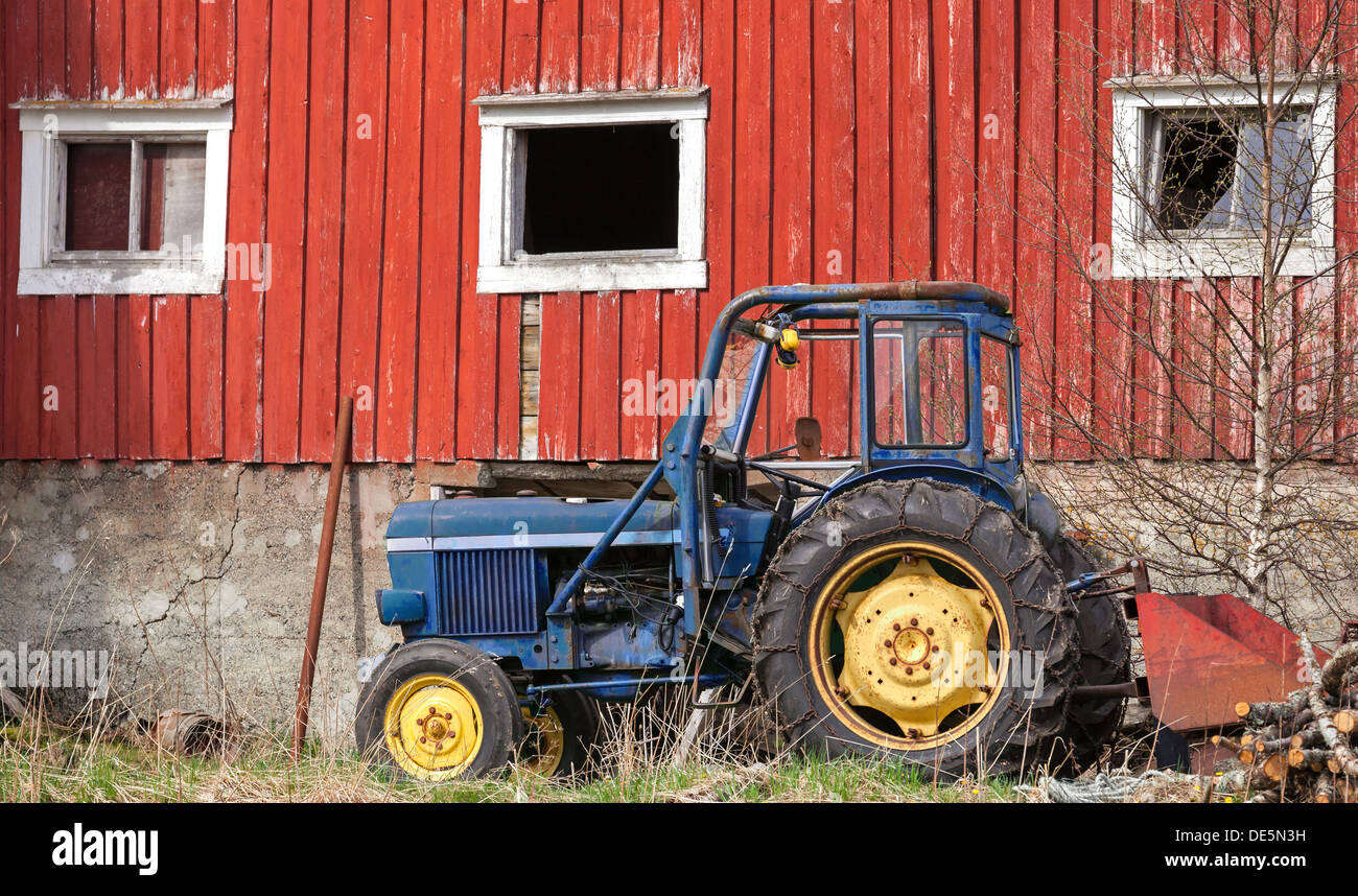 Small blue tractor stands on grass nearby red barn wall in Norway Stock Photo