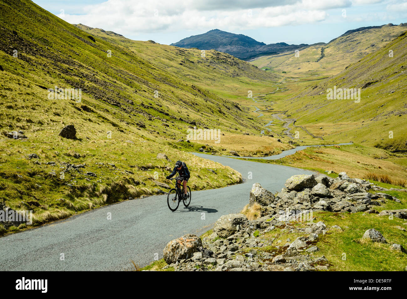 Cyclist climbing the steep west side of Wrynose Pass in the English Lake District with Harter Fell behind Stock Photo