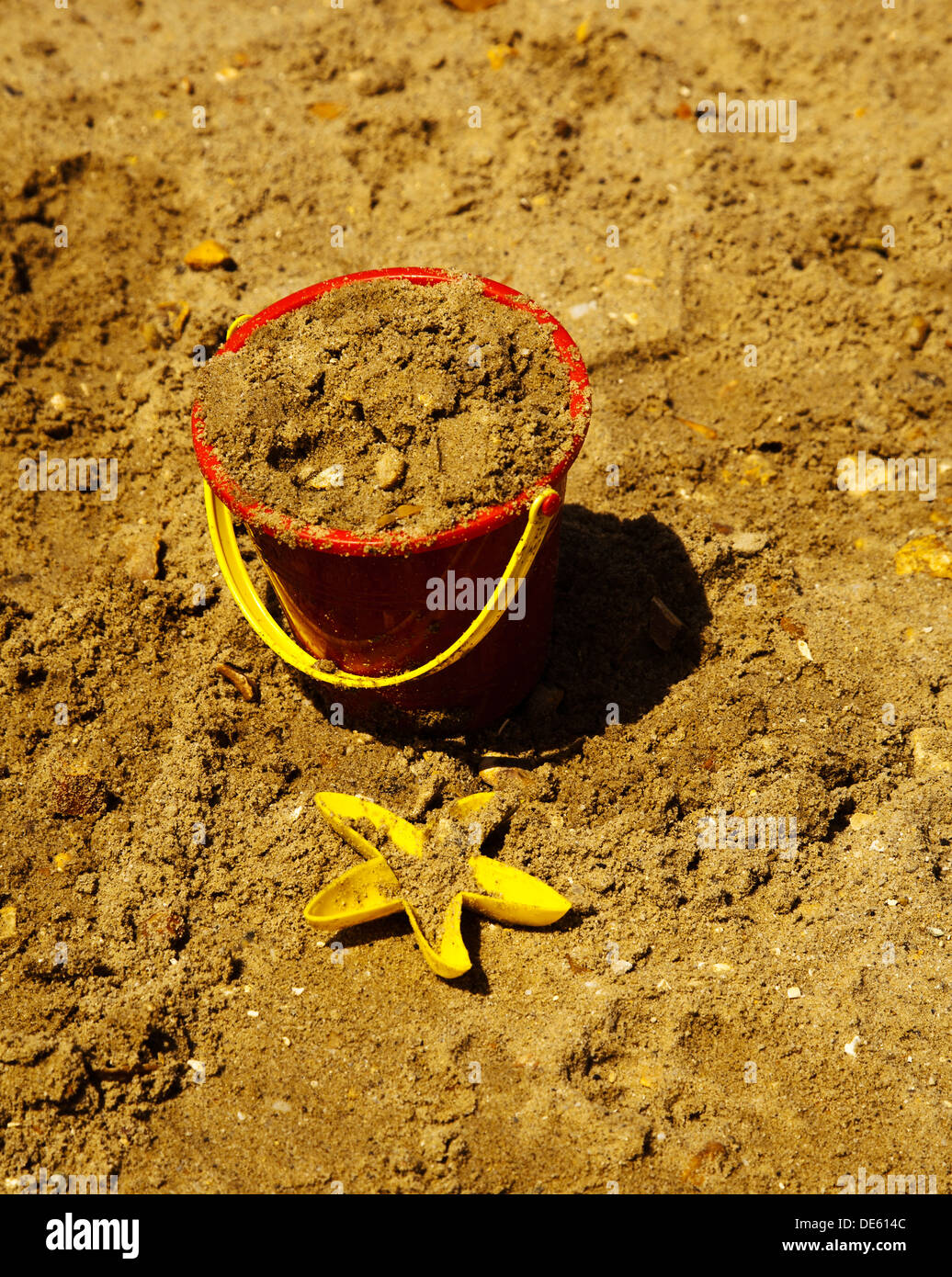 A child's sand filled bucket and yellow plastic starfish on the beach Stock Photo