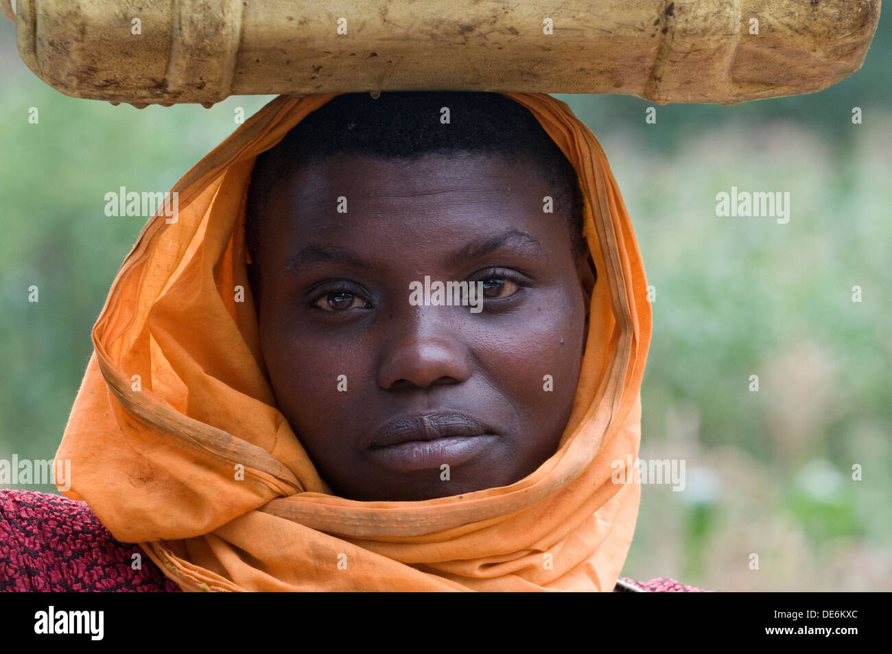 Serenely beautiful Rwandan woman leaving well with traditional headscarf and water container Virunga Lake Burera Central Rwanda Stock Photo