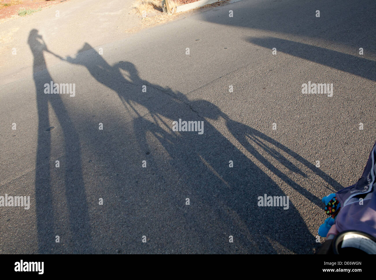 Shadow silhouette of a mother pushing a baby in stroller at sunset. Stock Photo