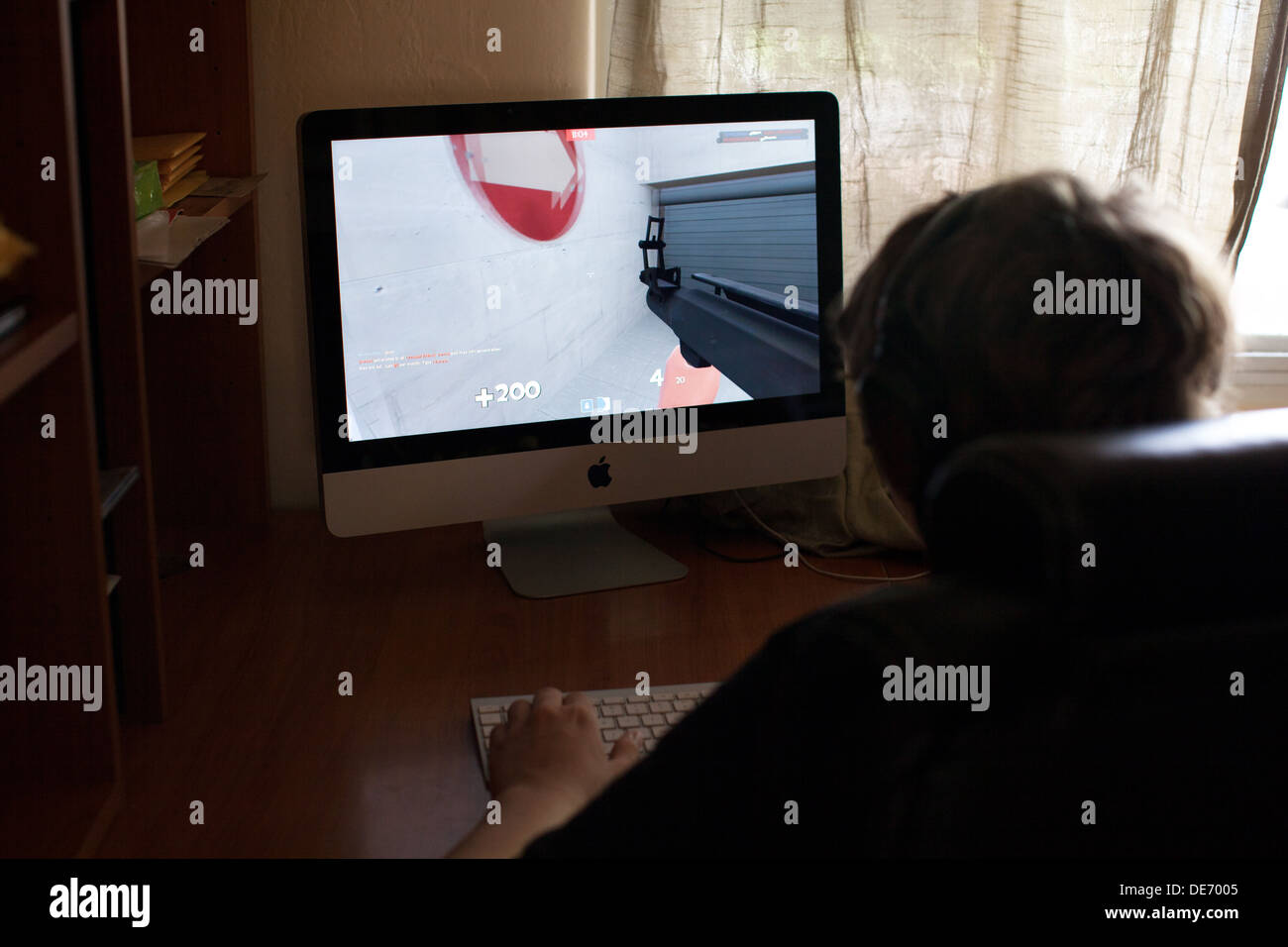 Teenage boy plays online video game, Team Fortress Two, at home on computer while interacting with other players via Skype Stock Photo