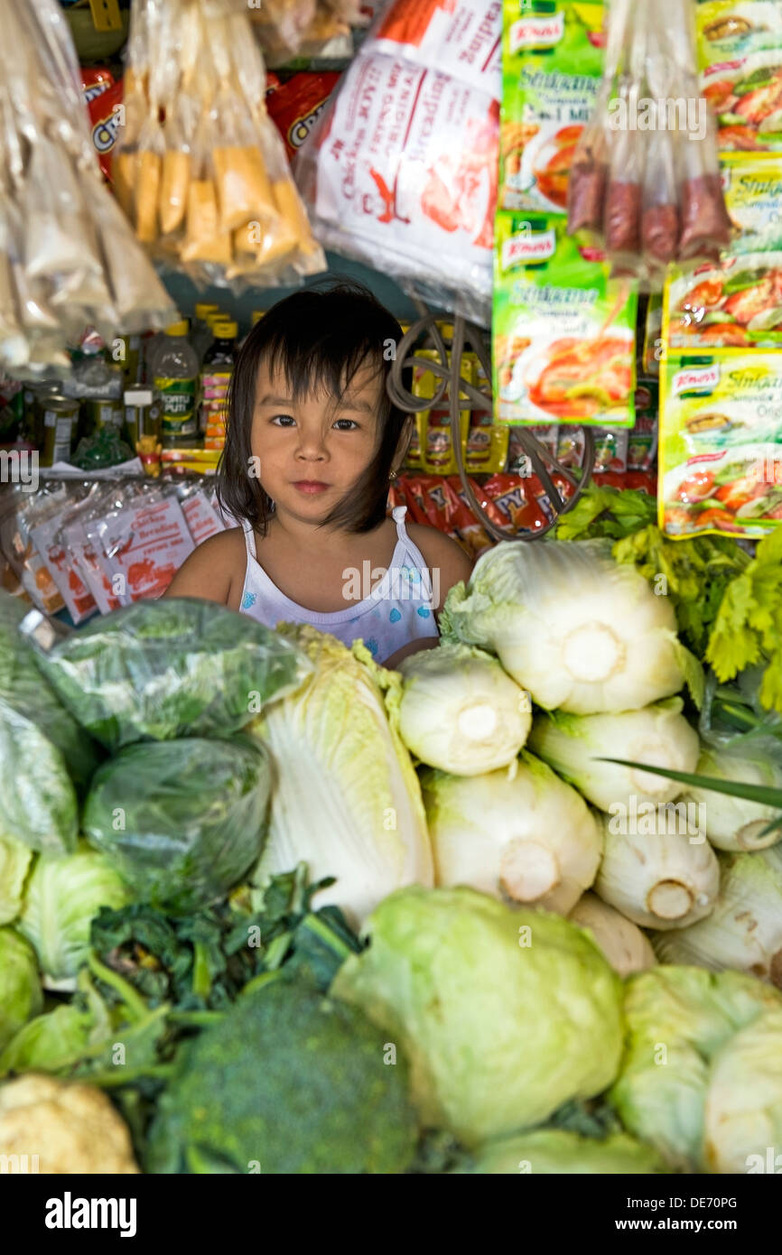 A beautiful, young Filipino girl helping her parents sell vegetables and supplies at a public market in the Philippine Islands. Stock Photo