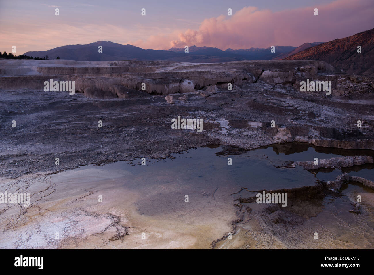Photograph of the sunset over Mammoth Hot Springs with a plume of smoke from a wildfire in the background. Stock Photo