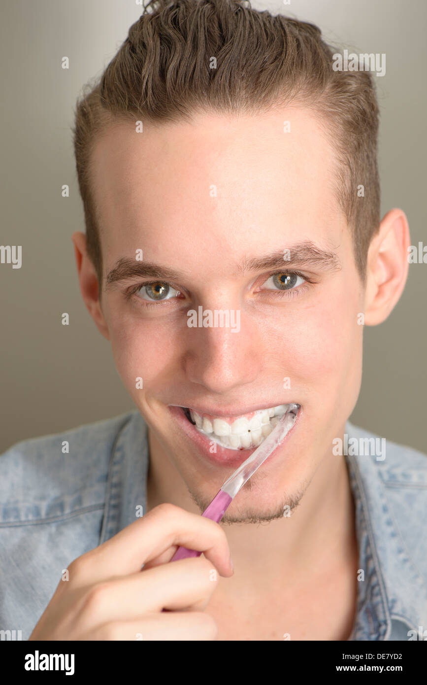 Lifestyle portrait of happy young man brushing his teeth with a pink toothbrush Stock Photo