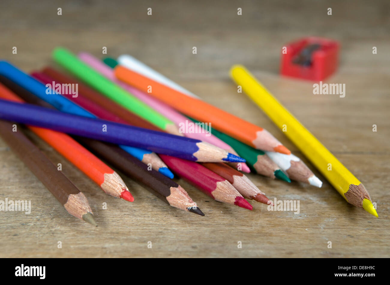 Colouring pencils with sharpener on old wooden desk top Stock Photo
