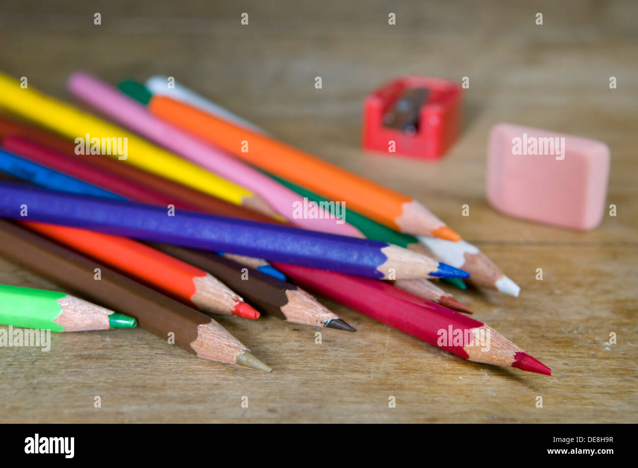 Colouring pencils with sharpener and rubber on old wooden desk top