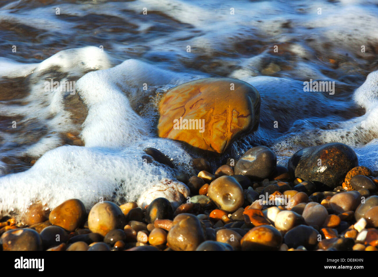 Incoming tide laps around rocks on the shingle beach at Sidmouth, Devon on the Jurassic Coast. Stock Photo