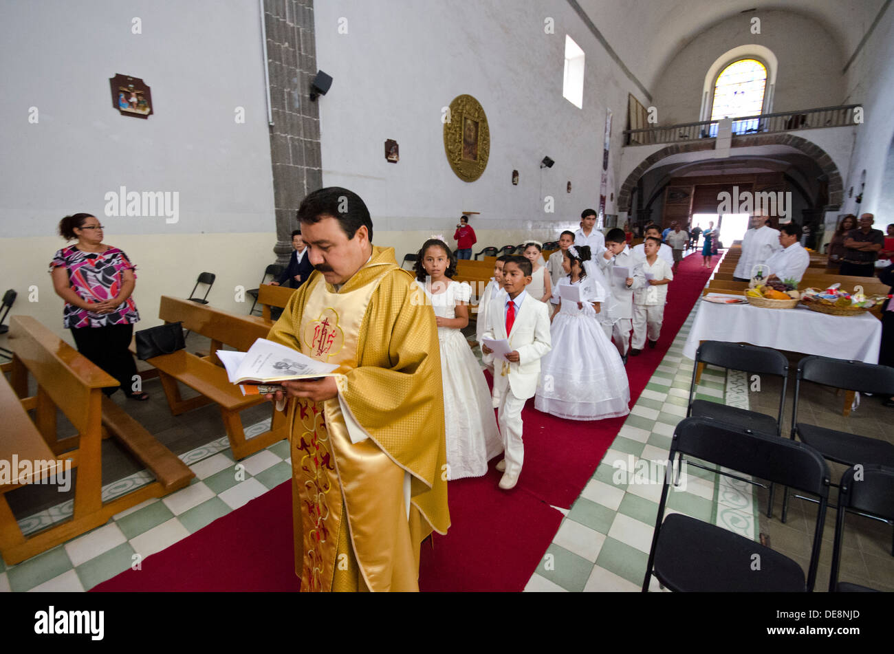 Catholic priest leads in young First Communicants into church in Tequisquiapan in Mexico Stock Photo